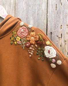 a close up of a person wearing a brown sweatshirt with flowers on it and a wooden background