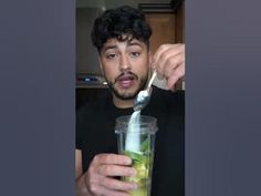 a man is holding a spoon in his hand and looking at the camera while he holds a drink