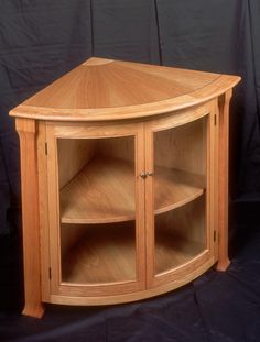 a wooden corner cabinet with glass doors on the top and bottom shelves, in front of a black background