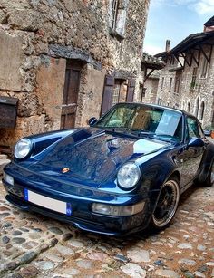 a blue sports car parked in front of an old stone building on a cobblestone street