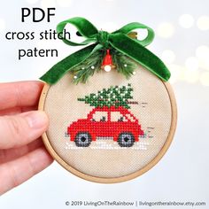 a cross stitch christmas ornament with a red car carrying a tree on it