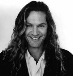 a black and white photo of a man with long curly hair smiling at the camera