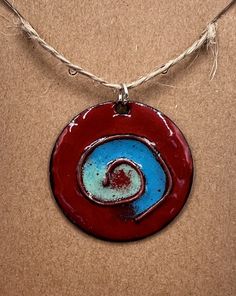 Blue & Red Enameled Copper Pendant This pendant is kiln fired enamel on copper.  It includes raw copper wire placed in an abstract shape. The pendant itself measures 1 inch in length and the width is approximately 1 inch at the widest point.  Listing is for pendant only, no chain included.  Handmade in my garage studio in Glen Allen, VA. Enameling is a process in which powdered glass is fused to a metal at high heat (generally between 1,400 and 1,650 degrees Fahrenheit). This piece started with a shape cut out of copper, referred to as a blank.  I source my blanks from various other Etsy shops and local stores in Richmond, VA.  The copper is cleaned and then a layer of counter enamel is applied to the back of the piece and fired in the kiln.  The counter enamel helps to keep the piece from Artsy Red Jewelry For Gifts, Artsy Red Necklace For Gift, Red Spiral Jewelry As Gift, Spiral Shaped Red Jewelry For Gifts, Red Spiral Jewelry For Gifts, Round Enamel Pendant Jewelry With Polished Finish, Artsy Red Nickel-free Jewelry, Red Enamel Necklace Nickel Free, Artisan Enamel Round Pendant Jewelry