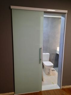 an open door leading to a bathroom with a toilet in the corner and wood flooring