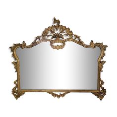 an ornate gold framed mirror on a white wall with leaves and scrolls around the edges