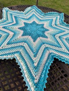 a crocheted blue and white star is on a black metal table in the grass