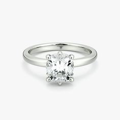 a white gold engagement ring with a round cut diamond in the center, on a plain surface