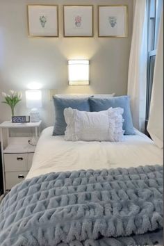 a white bed with blue pillows and blankets on it in front of three framed pictures