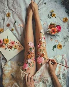 a woman laying on top of a bed covered in flowers and holding a paintbrush