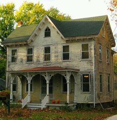 an old wooden house with porches and stairs in the fall leaves on the ground