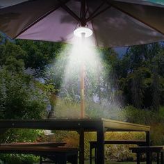 an open umbrella with the light shining on it in front of some picnic tables and benches