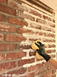 a brick wall being painted yellow and black by a person with gloved hands on it