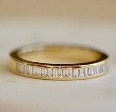 a gold wedding band with baguetts of diamonds on the side, sitting on a white surface