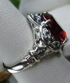 <> Made To Order This is a Gothic/Vintage revival solid sterling silver crown filigree 5ct simulated red ruby ring. The round full cut Man-made red ruby gemstone is 12mm (just shy of 1/2th of an inch) in diameter. The gemstone has great colors (greens, purples, pinks, yellow, blues, etc)... The inside of the band is marked 925 for sterling. The ring sits 18mm NS on the finger. Notice the beautiful intricate swirl design of the silver filigree setting and band. This is a lovely new, well ma Red Ruby Ring, Ruby Bands, Vintage Revival, Gothic Revival, Gothic Vintage, Silver Crown, Filigree Ring, Swirl Design, Ruby Gemstone