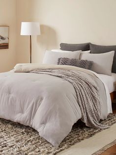 a bed with white sheets and pillows in a bedroom next to a lamp on a table