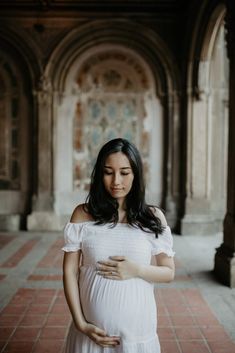 a pregnant woman standing in an archway with her hand on her belly