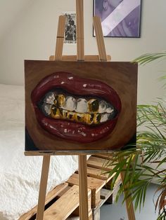 an easel with a painting of a mouth and teeth on it in front of a bed