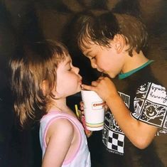 two young children standing next to each other and one is holding a coffee cup in his mouth