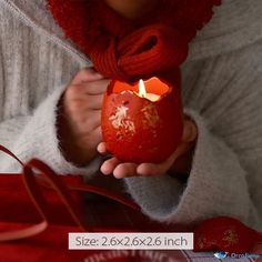 a woman holding a red candle in her hand and wearing a white sweater over it