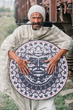 a man holding a plate with an image of a face on it, while standing next to a train