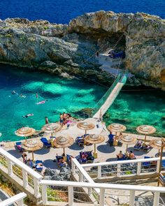 people are swimming in the clear blue water next to umbrellas and steps leading up to an overhang