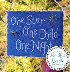 a cross stitch ornament hanging from a christmas tree with the words one step, one child, one night