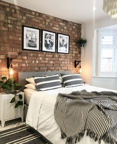 a bedroom with brick wall and white bedding, two pictures on the wall above it