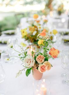 an arrangement of flowers in a vase on a long table with wine glasses and candles