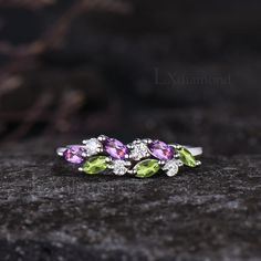 three different colored stones on top of each other in a ring with diamonds and green leaves