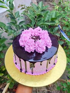 a chocolate cake with pink flowers on top sitting on a yellow plate in front of some bushes