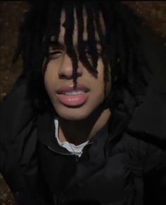 a young man with dreadlocks on his face wearing a black jacket and white shirt