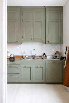 an open kitchen with green cabinets and white tile backsplash, wood flooring