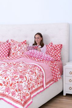 a woman is sitting on her bed looking at the pillows and quilts she has made