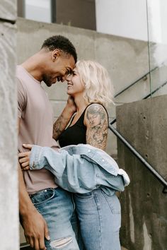 a man and woman standing next to each other in front of some stairs with their arms around each other