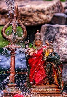 a fountain with water pouring out of it and two statues on the side, surrounded by rocks