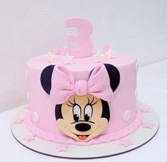 a pink birthday cake decorated with minnie mouse's face and the number 3 on top