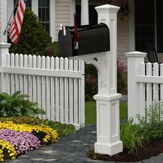 a mailbox in front of a white picket fence with flowers and an american flag