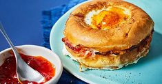 a breakfast sandwich with an egg in the middle on a blue plate next to a bowl of jelly