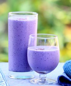 two glasses filled with purple liquid sitting next to each other on a blue table cloth