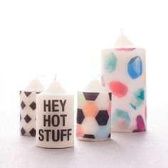 three candles with different designs on them sitting next to each other, one candle has the word hey hot stuff written on it