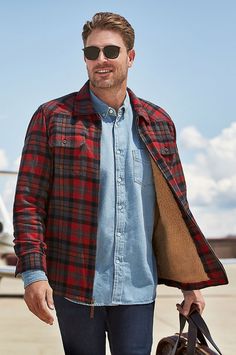 a man with sunglasses and a plaid shirt is holding a handbag while standing in front of an airplane