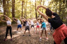 a group of people standing in a forest doing stretching exercises with their hands up to the side