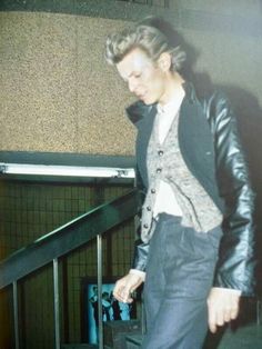 a young man is walking down the stairs with his luggage in hand and wearing a black leather jacket