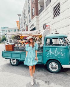 a woman standing in front of an old truck with flowers on the back and awning