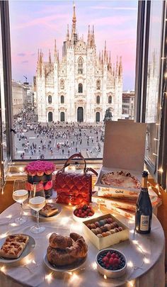 a table topped with lots of food next to a window filled with wine bottles and glasses