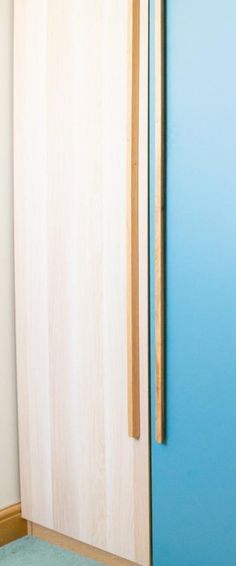 a blue door with a wooden handle next to a white wall and bed in a room