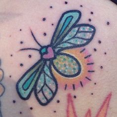 a colorful dragonfly tattoo on the back of a woman's shoulder