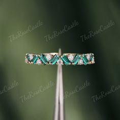 a diamond and emerald ring sitting on top of a piece of metal with diamonds in it