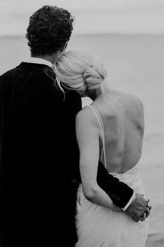 a man and woman standing next to each other near the ocean on their wedding day