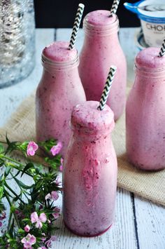 three pink smoothies with straws in them sitting on a table next to some flowers